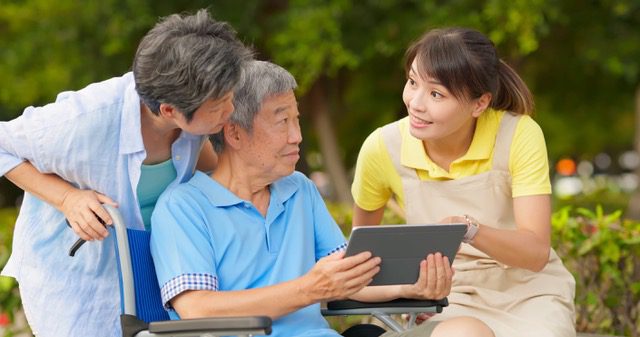 A Woman Standing Beside the Elderly Man Holding a Tablet<br />
